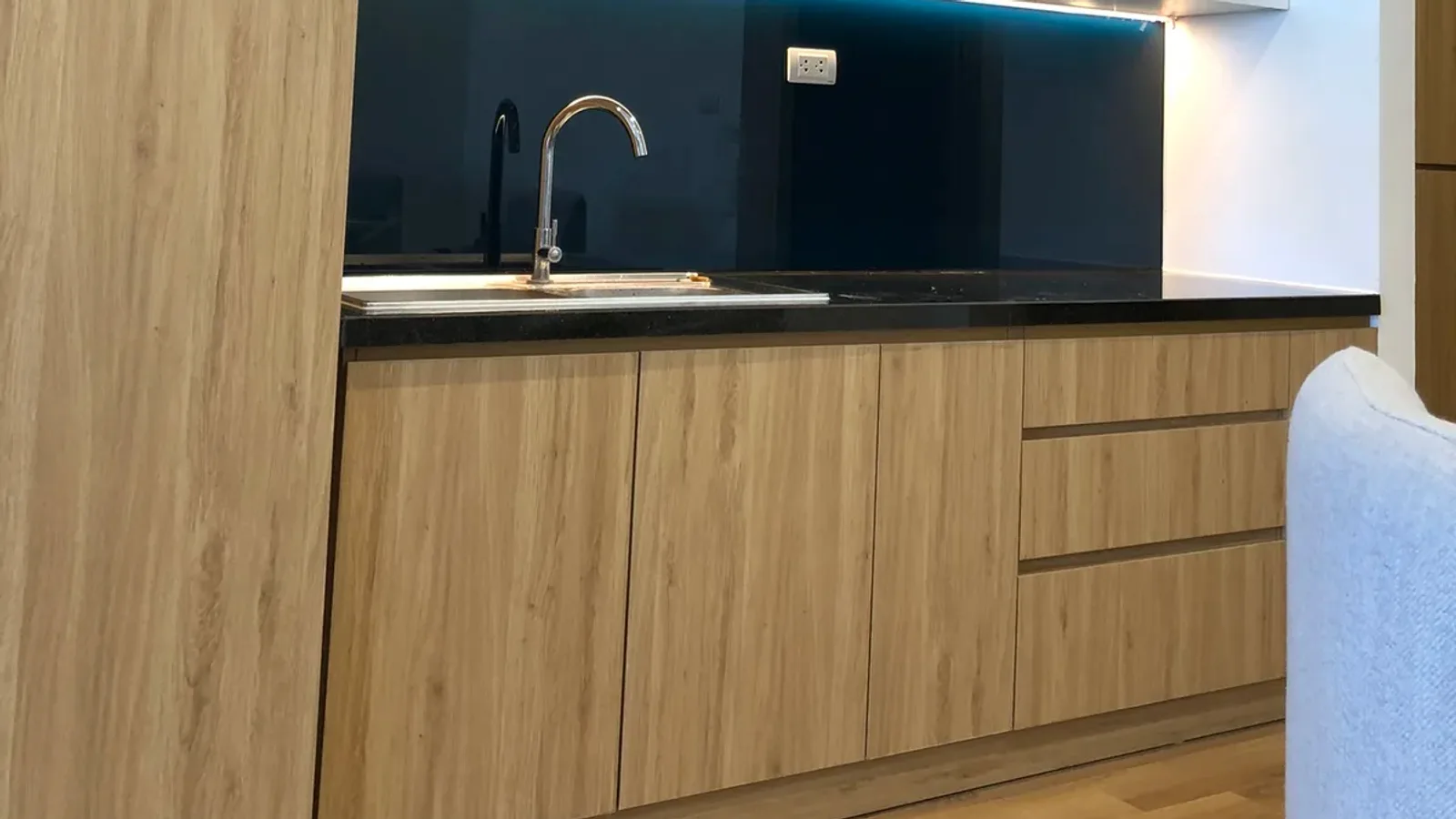 Tủ bếp dưới cánh vân gỗ sáng, mặt đá đen và khoang chậu rửa trong căn hộ studio TMS Quy Nhơn do WOTU đóng tại xưởng Hoa Lư