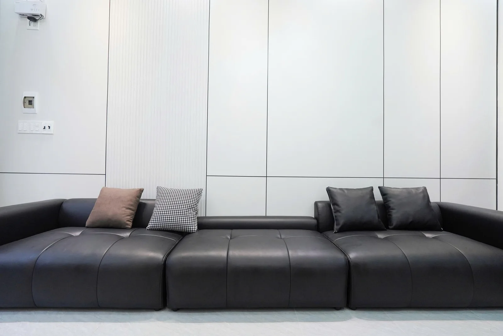Sofa da đen đặt trước mảng ốp tường trắng rãnh dọc kịch trần
